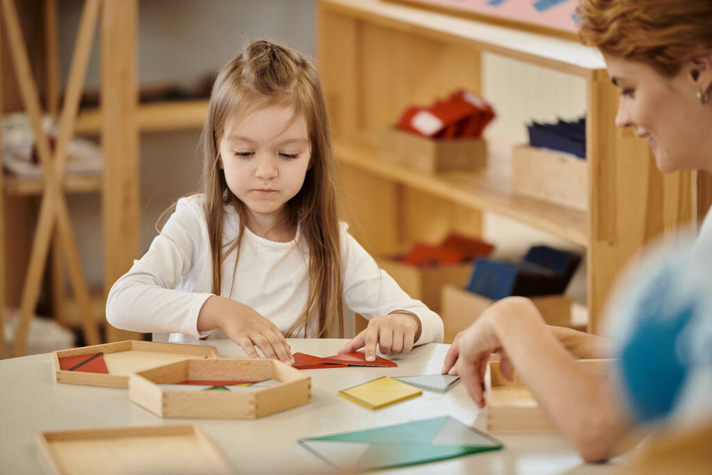 usmívající se učitel hrát s dívkou a didaktický materiál na stole v Montessori škole - Fotografie, Obrázek