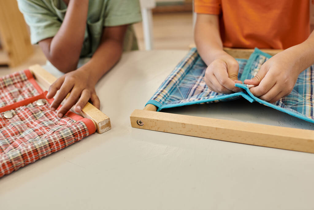 przycięty widok wieloetnicznych dzieci bawiących się tkaniną i guzikami podczas lekcji w szkole montessori - Zdjęcie, obraz