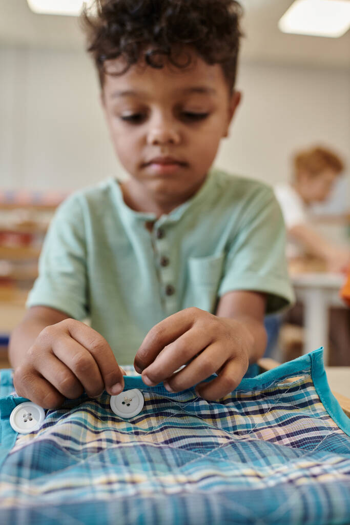 Bulanık Afrikalı Amerikalı çocuk Montessori okulunda kumaş ve düğmelerle oynuyor. - Fotoğraf, Görsel