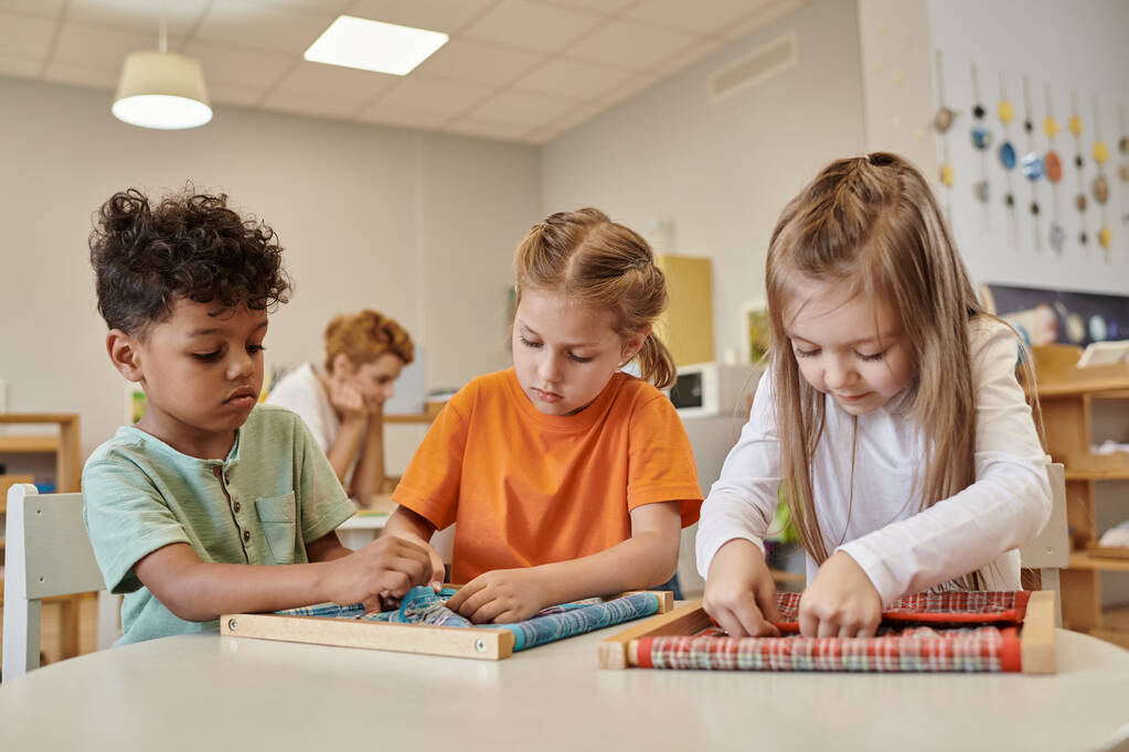 wielonarodowe dzieci bawiące się tkaniną i guzikami na stole w szkole Montessori - Zdjęcie, obraz