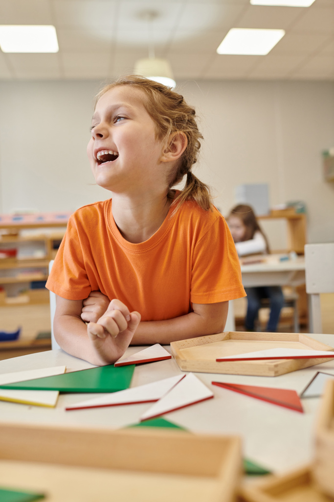 щаслива дитина дивиться далеко біля дерев'яних дидактичних матеріалів у класі школи Монтессорі - Фото, зображення