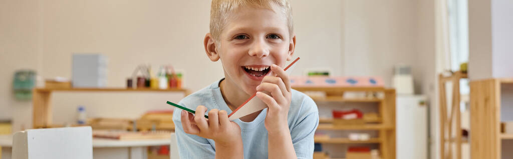 cheerful boy holding triangles during game in classroom in montessori school, banner - Photo, Image