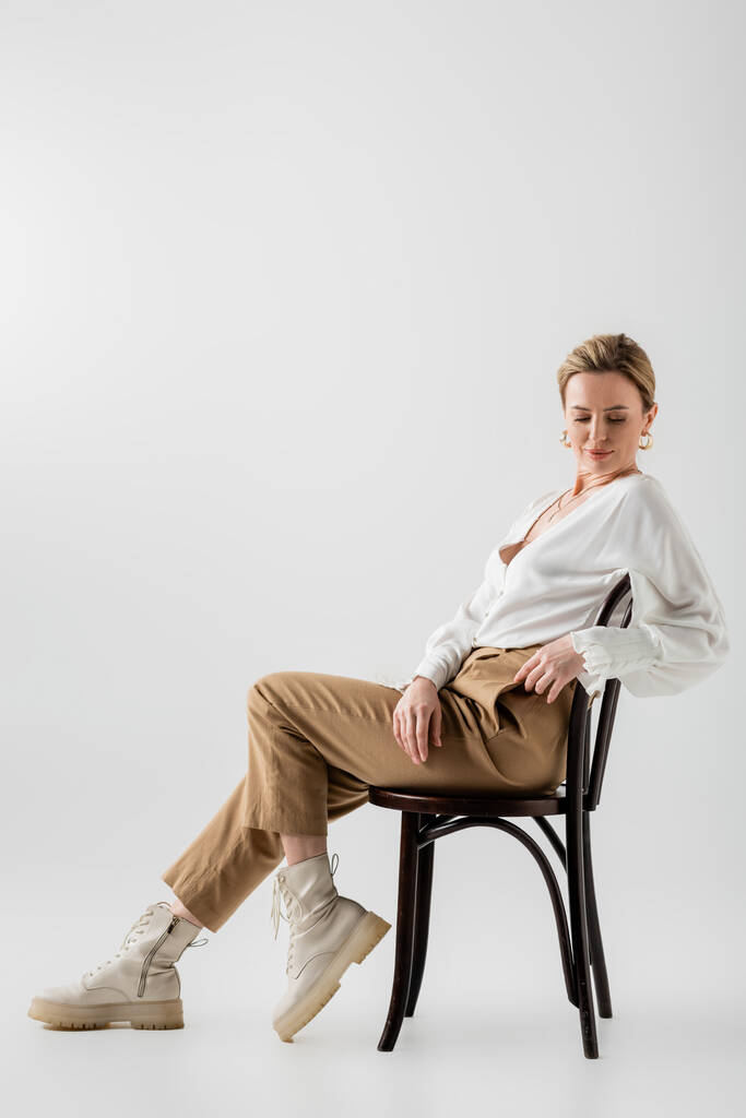 mulher loira elegante em traje formal elegante sentado na cadeira e relaxante, estilo e moda - Foto, Imagem