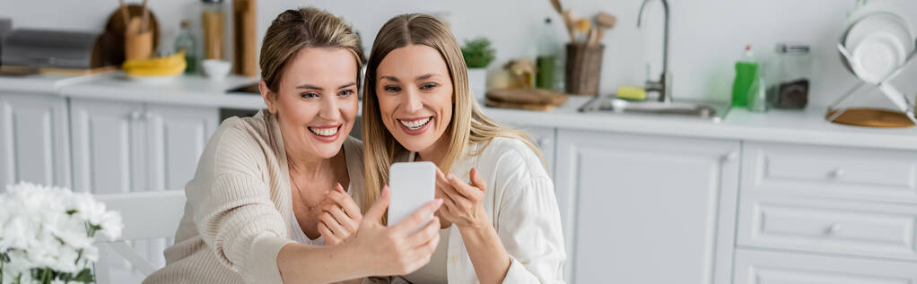 dwie blondynki siostry w pięknym stroju podejmowania selfie na tle kuchni, rodzinna więź, baner - Zdjęcie, obraz