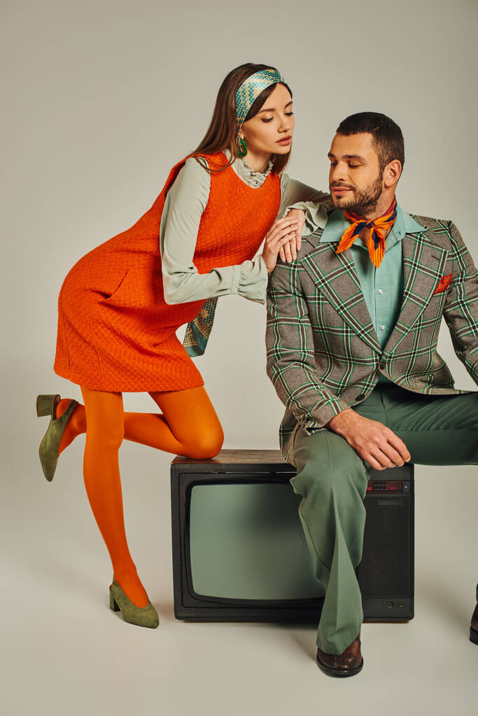 encantadora mulher inclinada no ombro do homem sentado na tv vintage em cinza, casal retro na moda - Foto, Imagem