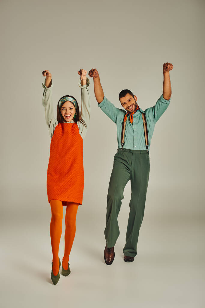 pareja alegre en ropa vintage bailando con las manos levantadas en gris, felicidad y vibraciones retro - Foto, imagen