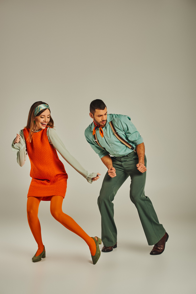 in voller Länge junge modische Paar in bunten Retro-Kleidung tanzen auf grau, Spaß und Aufregung - Foto, Bild
