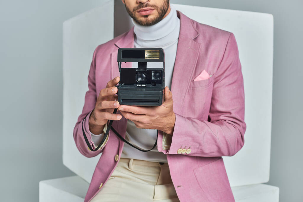 cropped view of modern man in lilac blazer taking photo on vintage camera near white cubes on grey - Photo, Image
