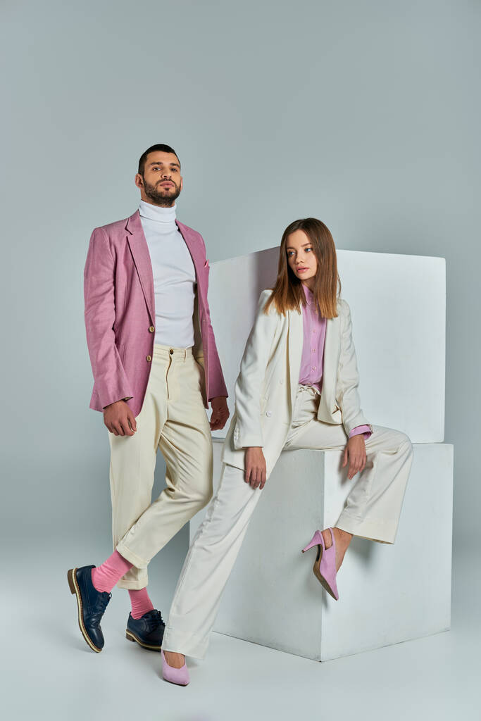 Modernes Paar in pastellfarbener Businesskleidung posiert neben weißen Würfeln auf grauen, jungen Profis - Foto, Bild