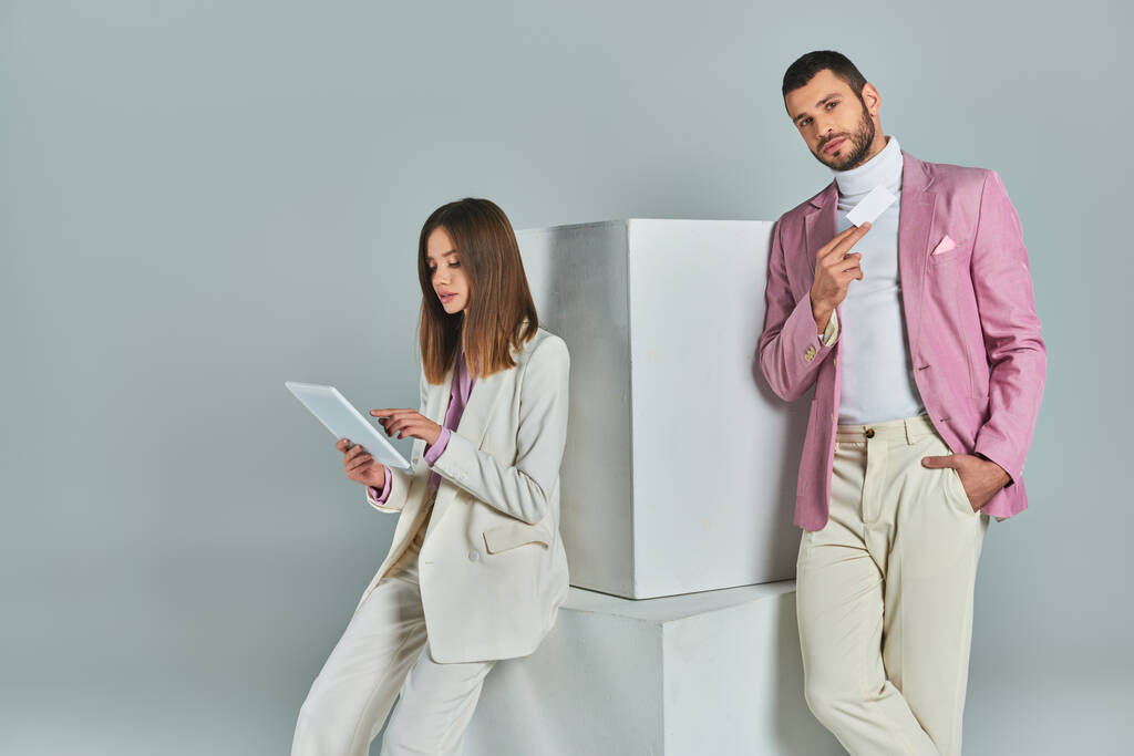 ζευγάρι με κομψό επίσημο ένδυμα με ψηφιακό tablet και άδεια επαγγελματική κάρτα κοντά σε λευκούς κύβους σε γκρι - Φωτογραφία, εικόνα