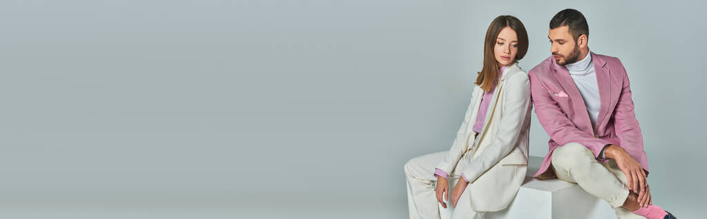 nuori bisnespari tyylikkäissä puvuissa istuu valkoisella kuutiolla harmaalla taustalla studiossa, banneri - Valokuva, kuva