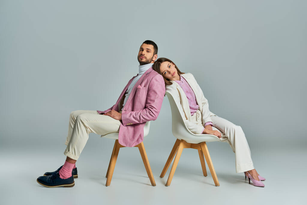 fiatal pár elegáns formális viselet ül háttal fotelekben és nézi kamera szürke - Fotó, kép