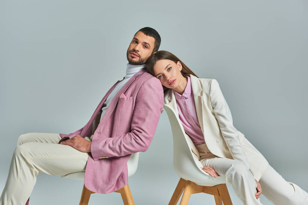Elegantes Paar in formeller Kleidung sitzt in Sesseln und blickt in die Kamera auf graue, moderne Mode - Foto, Bild