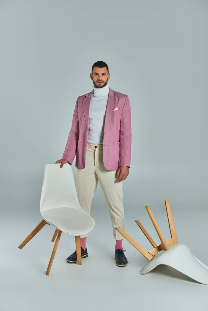 full length of man in lilac blazer and white pants posing with armchairs on grey, fashion and style - Photo, Image