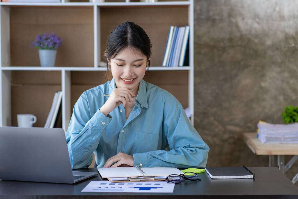 Azjatka korzystająca z laptopa i pracująca w biurze z kalkulatorem dokumenty finansowe na stole Planowanie analizy raportów finansowych w biurze - Zdjęcie, obraz