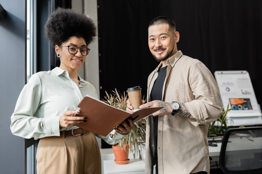asian businessman with coffee and african american businesswoman looking at camera in office - Photo, Image