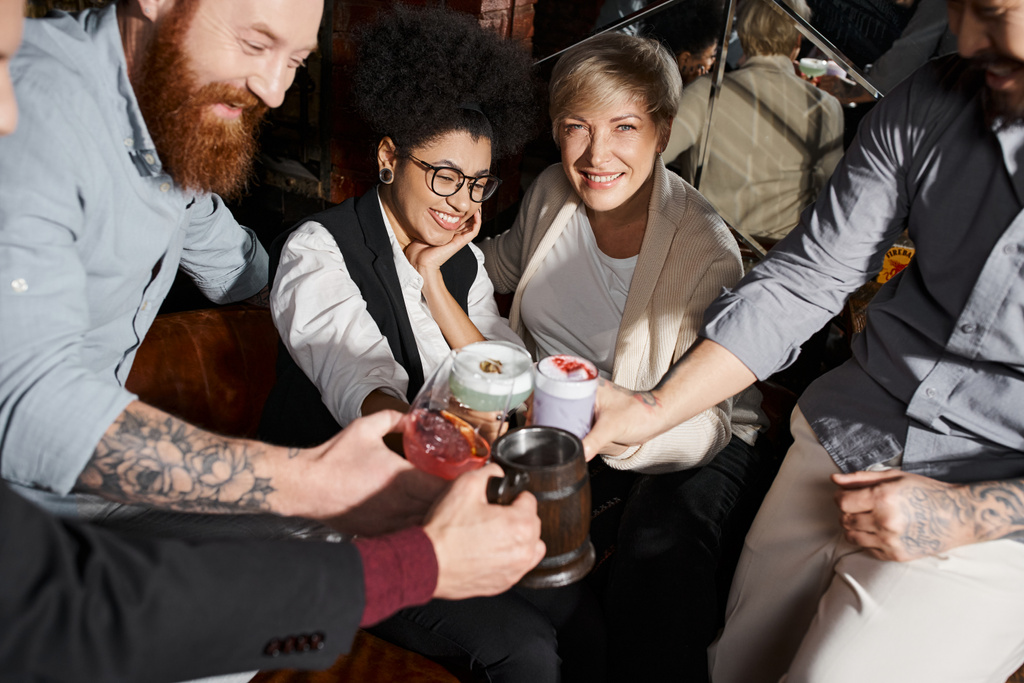 веселые мультиэтнические коллеги звонят в стаканы с коктейлями, веселясь в баре после работы - Фото, изображение
