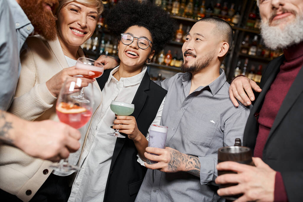 usmívající se multietničtí kolegové držící sklenice s alkoholickými nápoji, zatímco tráví čas v baru - Fotografie, Obrázek