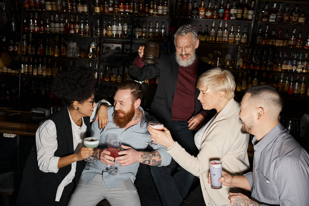 joyful african american woman and bearded man talking near multiethnic workmates with drinks in bar - Photo, Image