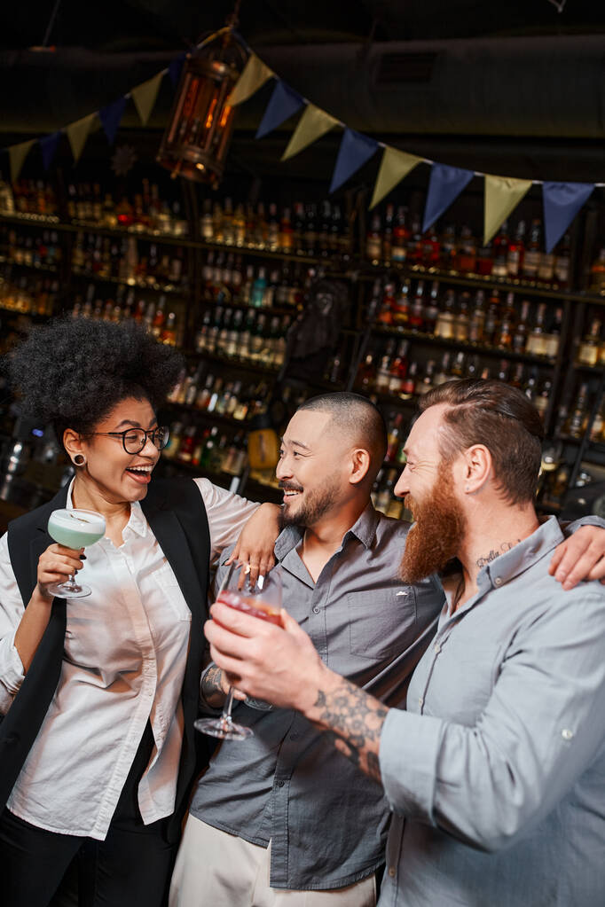 バーでのワークパーティーの後,アフリカ系アメリカ人女性を笑い見ている多民族のひげ付き男性 - 写真・画像
