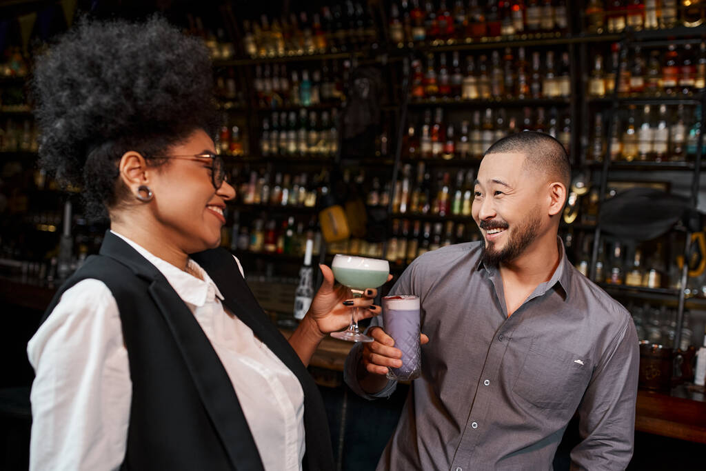 Africano americano mulher e asiático homem com bebidas sorrindo durante conversa no cocktail bar, - Foto, Imagem