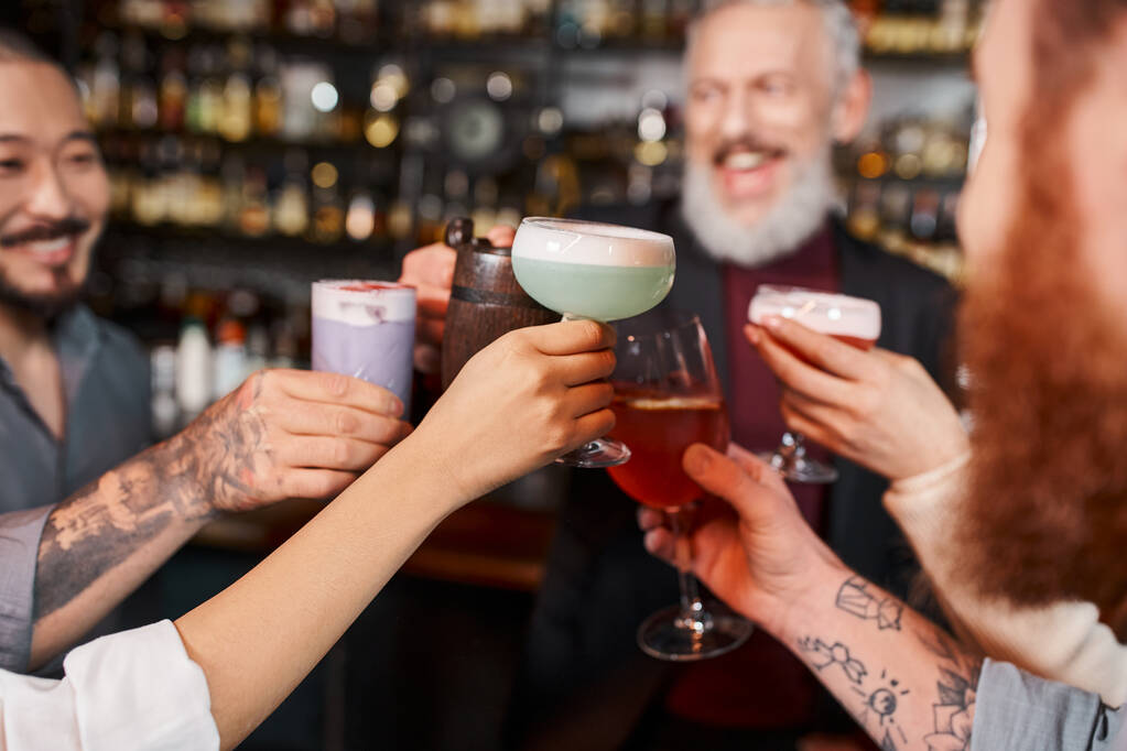 örömteli többnemzetiségű munkatársak koccintás poharak koktélokkal a bárban munka után, homályos háttér - Fotó, kép