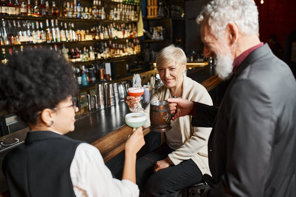 mulheres multiétnicas positivas e homem barbudo relaxando no bar de coquetéis após o trabalho, festa corporativa - Foto, Imagem