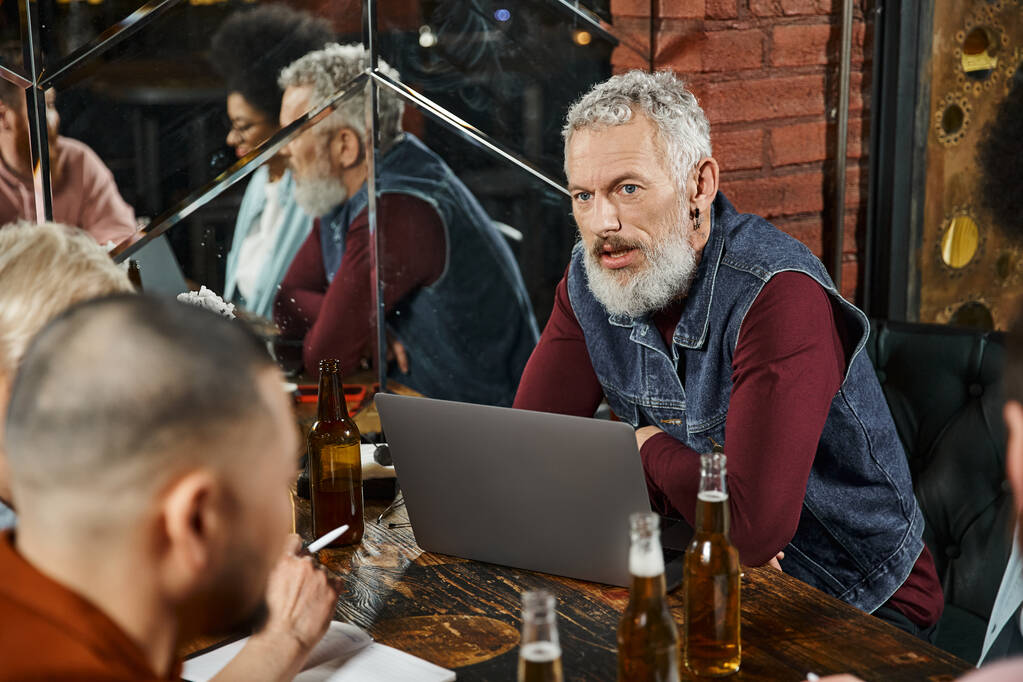 szakállas férfi ül közel laptop és megvitatása startup projekt multietnikus csapat bárban - Fotó, kép