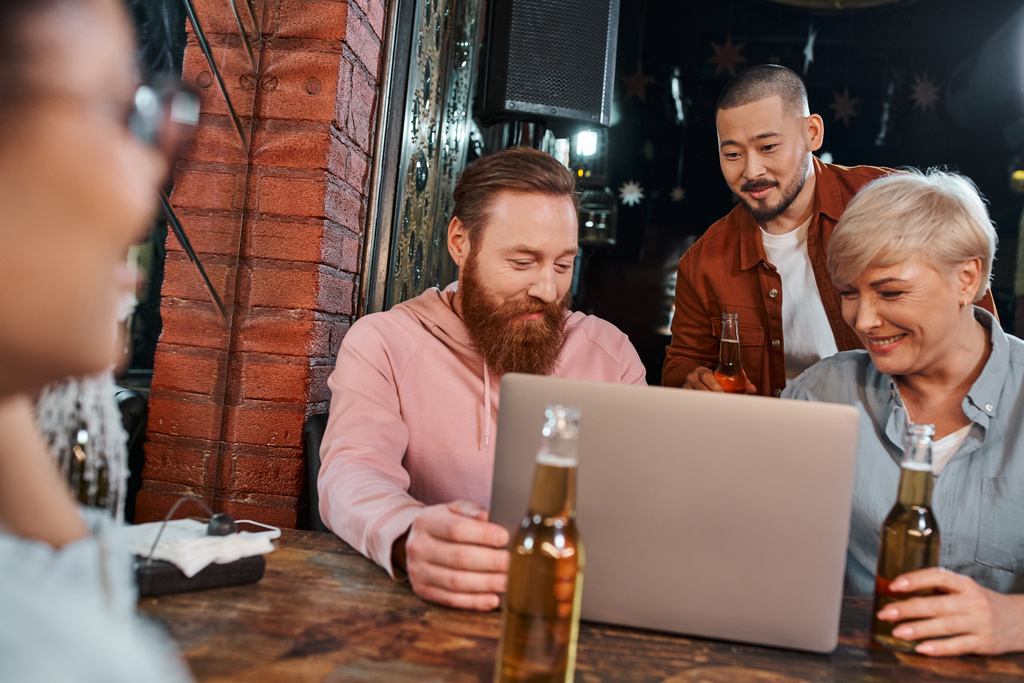 hymyilevät monikansalliset kollegat katselevat kannettavaa tietokonetta suunnitellessaan uutta projektia pubissa - Valokuva, kuva