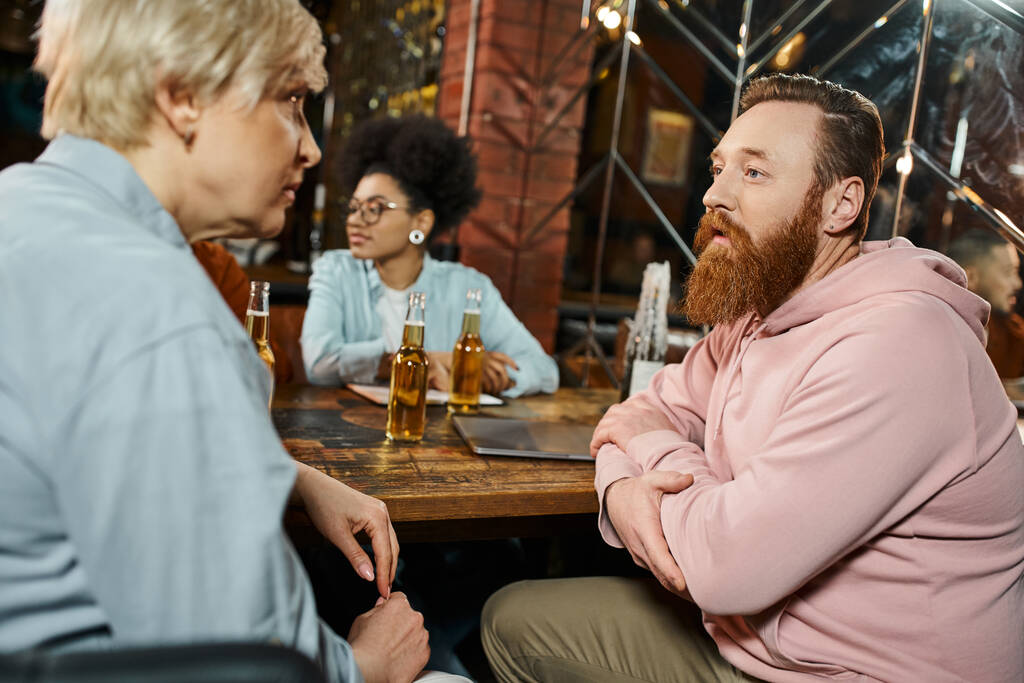 homme barbu et femme d'âge moyen parlant près d'un collègue afro-américain lors d'une réunion dans un pub - Photo, image