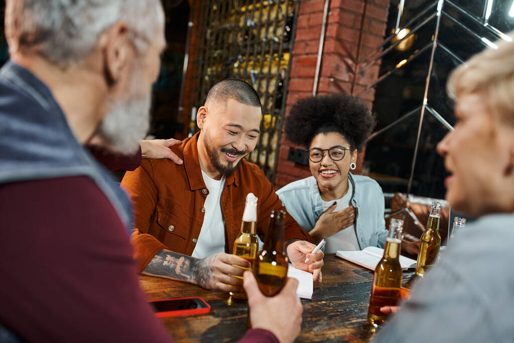 iloiset monikansalliset työkaverit, joilla on olutpulloja ja puhuvat uudesta liikehankkeesta pubissa - Valokuva, kuva