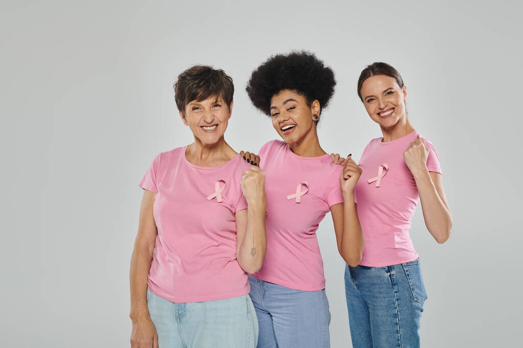 Brustkrebs-Bewusstsein, fröhliche multikulturelle Frauen, die vor grauem Hintergrund lächeln, verschiedene Generationen - Foto, Bild