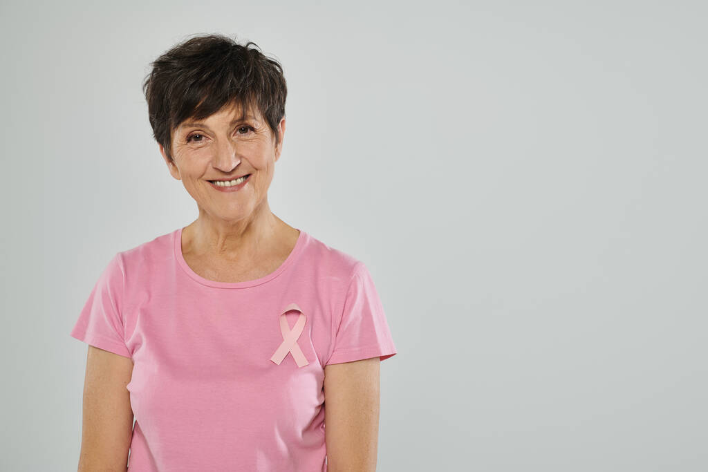обізнаність про рак молочної залози, щаслива жінка середнього віку з рожевою стрічкою, сірий фон, портрет - Фото, зображення
