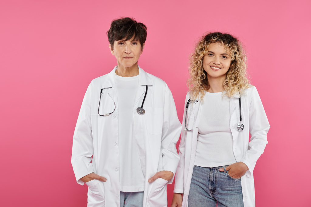 heureuses femmes médecins en manteaux blancs debout sur fond rose, sourire, sensibilisation au cancer du sein, femmes - Photo, image