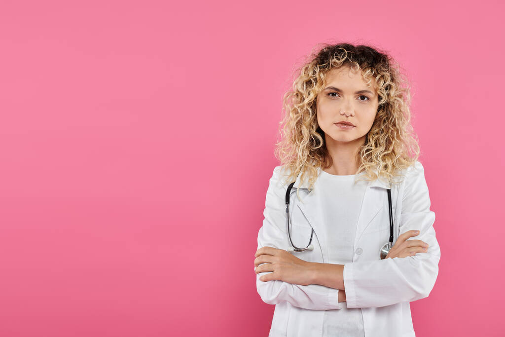 концепція обізнаності про рак молочної залози, кучерява жінка-лікар дивиться на камеру, рожевий фон, жінка - Фото, зображення
