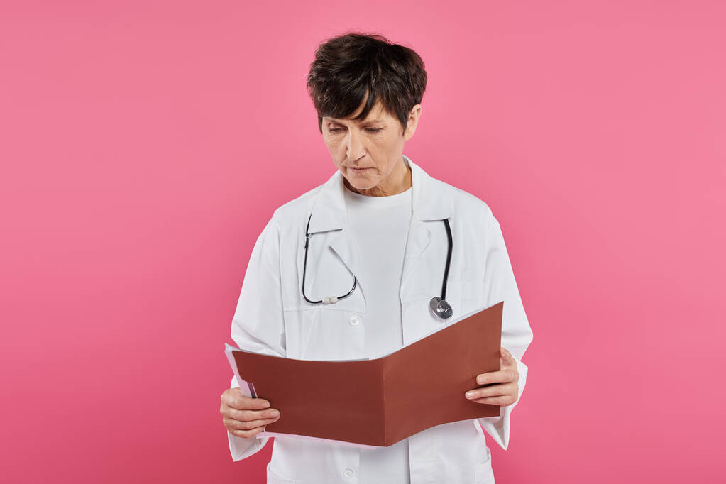 middle aged oncologist, female doctor looking at folder, breast cancer awareness concept, diagnosis - Photo, Image
