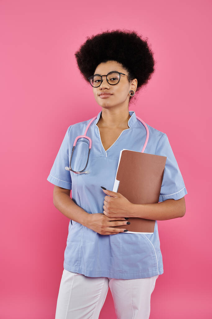 emlőrák tudatosság, afro-amerikai orvos, női onkológus mappával, rózsaszín háttér - Fotó, kép