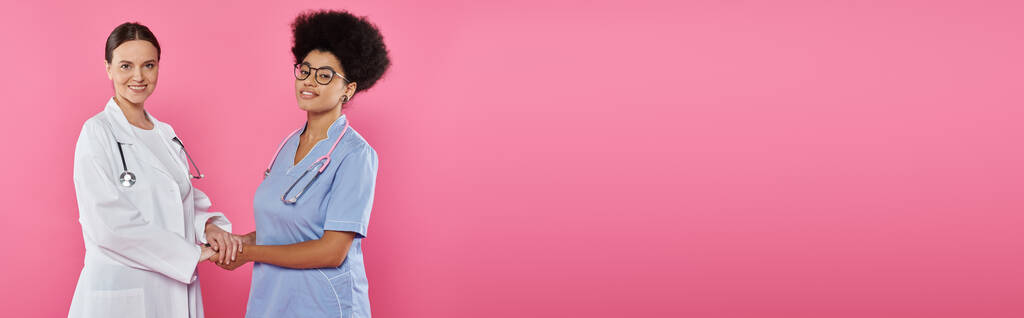 позитивні багатоетнічні лікарі тримають руки ізольовані на рожевому, банерному, концепції раку молочної залози - Фото, зображення