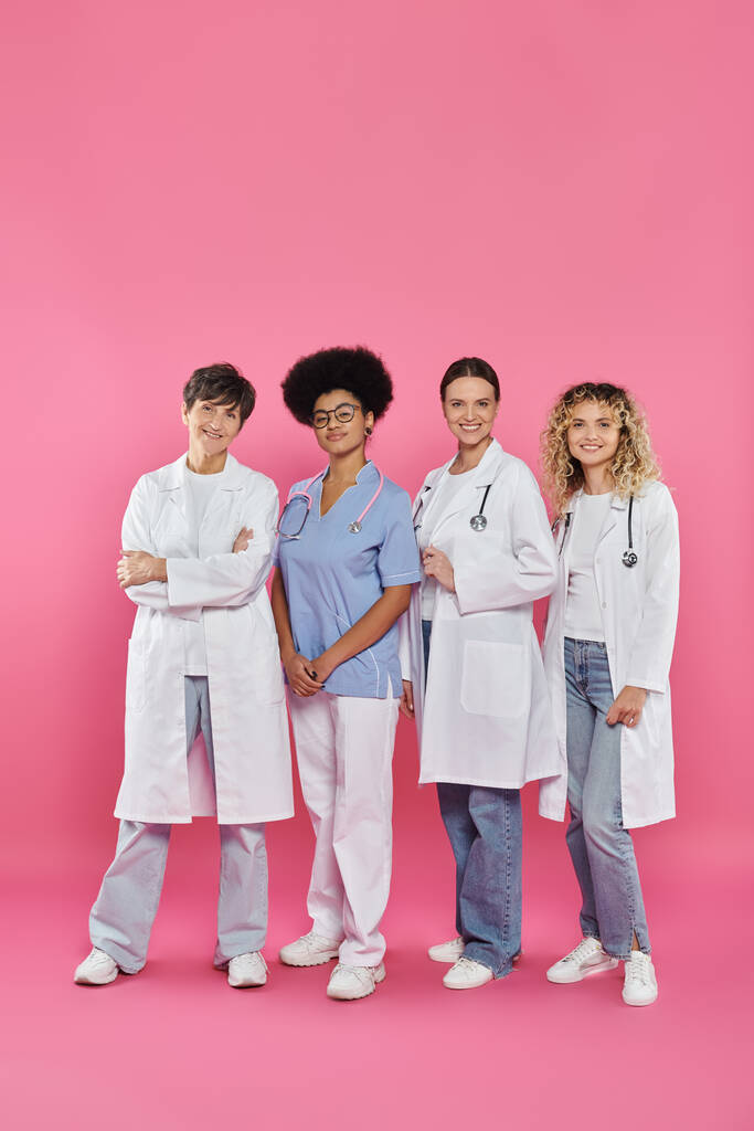 teljes hossza mosolygós fajok közötti orvosok állva együtt rózsaszín, mellrák hónap koncepció - Fotó, kép
