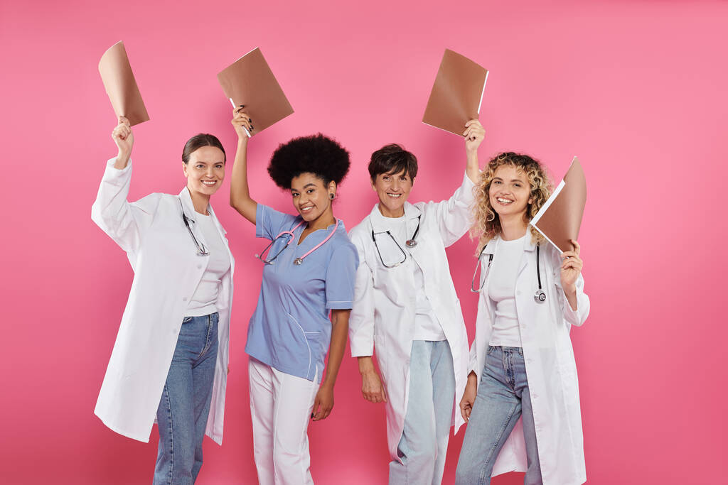 положительные межрасовые врачи держат бумажные папки изолированы на розовый, рак груди осведомленности - Фото, изображение