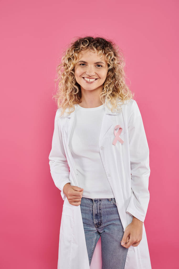 uśmiechnięty lekarz z wstążką na białym płaszczu wyizolowany na różowym, koncepcja raka piersi - Zdjęcie, obraz