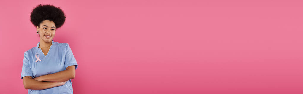 sonriente médico afroamericano con brazos cruzados de cinta aislados en rosa, cáncer de mama, pancarta - Foto, imagen