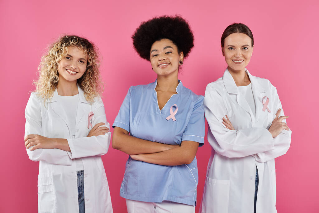 interracial doctors with ribbons crossing arms and smiling on pink, breast cancer concept - Photo, Image