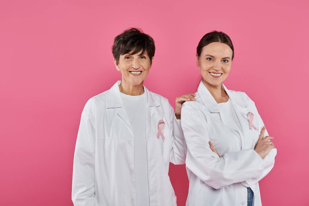 médicos positivos con cintas posando y de pie aislados en rosa, concepto de cáncer de mama - Foto, imagen