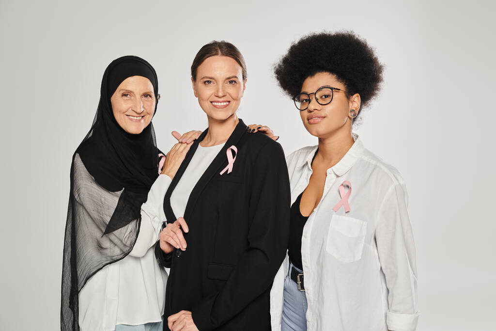 femmes souriantes interracial avec des rubans roses de cancer du sein étreignant isolé sur gris - Photo, image