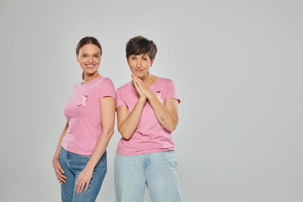 smiling women with pink ribbons and t-shirts standing isolated on grey, breast cancer - Photo, Image