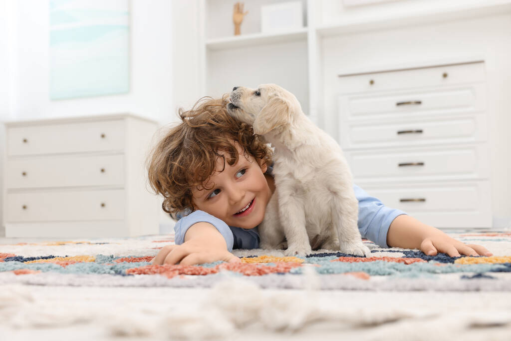Ragazzino sdraiato con cucciolo carino sul tappeto a casa - Foto, immagini