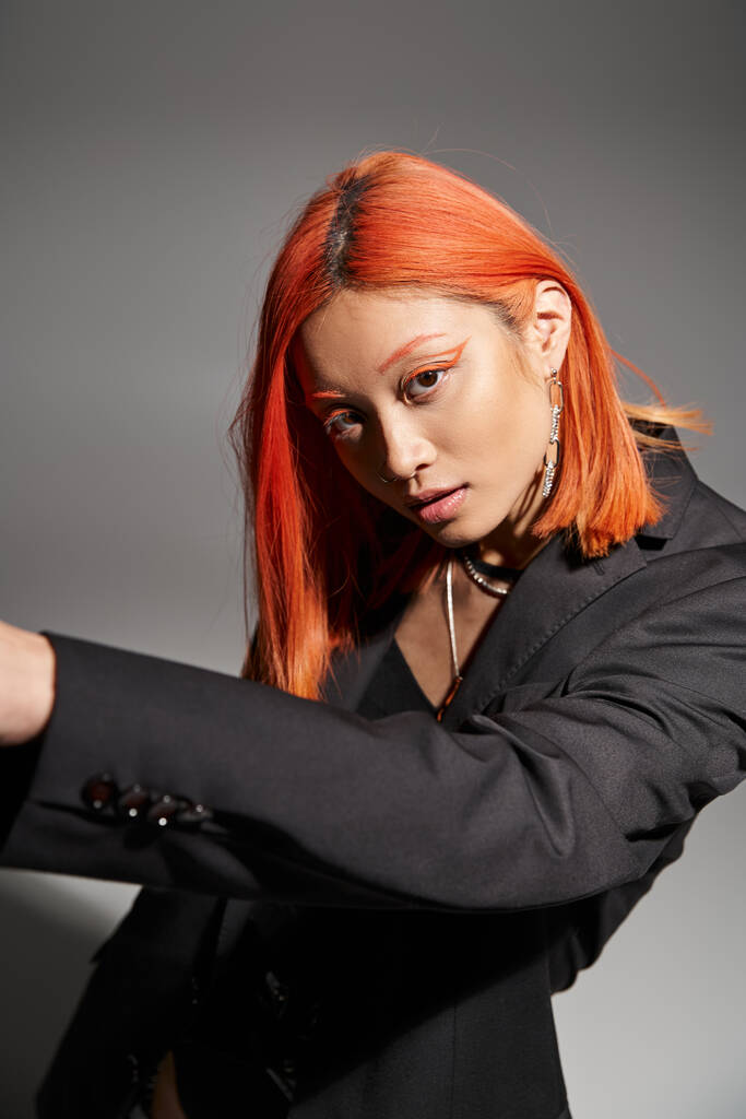asian woman with dyed hair and orange eye liner posing in black blazer on grey background, style - Photo, Image