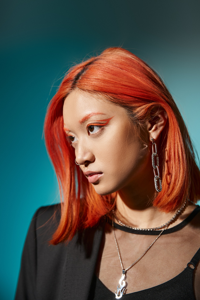 asian model with red hair and nose piercing posing in oversized blazer on blue backdrop, accessories - Photo, Image