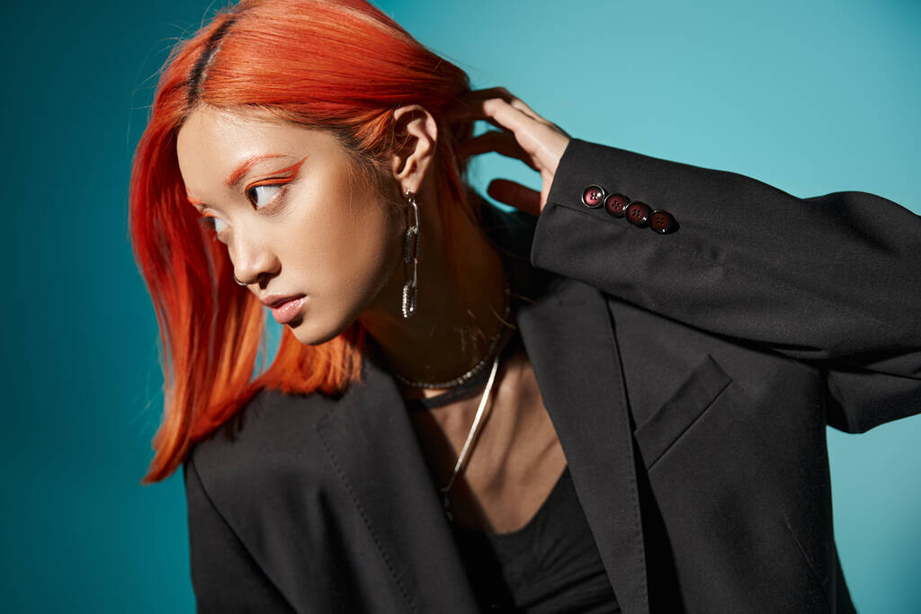 asian woman with red hair and nose piercing posing in oversized blazer on blue backdrop, accessories - Photo, Image
